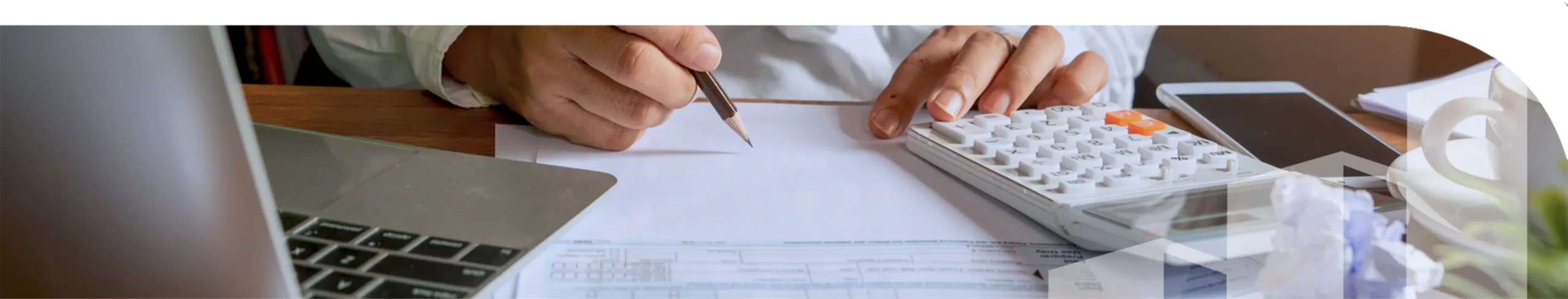 A man writing on a piece of paper with a calculator and laptop