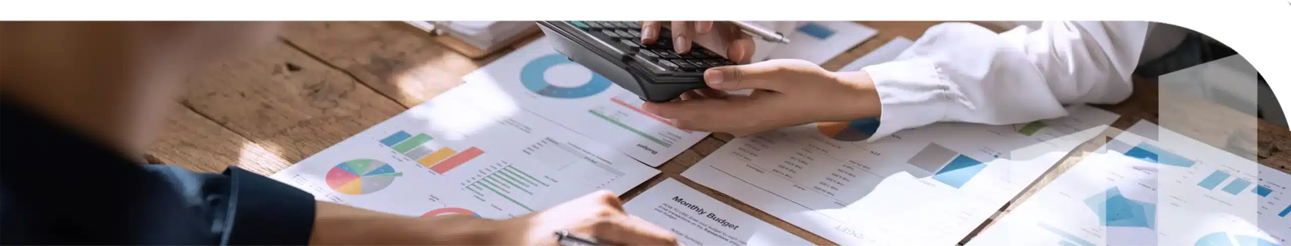 An image of papers with charts and a hand holding a calculator